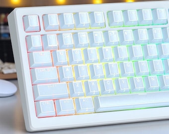 May include: A white mechanical keyboard with backlit keys. The keys are white with black lettering, and the backlighting transitions through a rainbow of colors. The keyboard has a minimalist design and a rectangular shape.