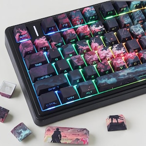 May include: A mechanical keyboard featuring custom keycaps with a dark, atmospheric landscape print in shades of black, pink, and blue. The keys are backlit with vibrant RGB lighting, and several loose keycaps with matching designs are placed nearby.