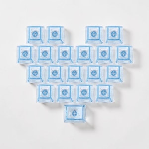 May include: Arrangement of clear, square-shaped objects with a blue cross design in the center. The objects are arranged in a heart shape against a white background. The objects appear to be made of plastic or glass.