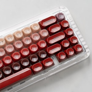 May include: A mechanical keyboard featuring a transparent acrylic frame and a gradient color scheme of round keycaps. The keys transition from light beige to deep red, with black lettering including Backspace, Enter, Shift, Menu, and Ctrl.