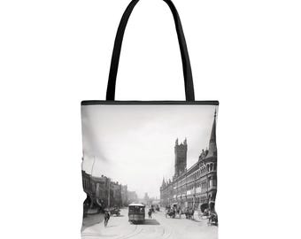 May include: A black and white photo of a city street scene with a streetcar in the middle of the road. The streetcar is surrounded by horse-drawn carriages and pedestrians. The buildings on either side of the street are tall and ornate.