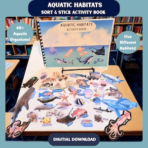 May include: An "Aquatic Habitats" activity book with various aquatic organisms and habitats. The book is open on a table, surrounded by colourful stickers of sea creatures like sharks, whales, and fish. Text on the cover reads "Aquatic Habitats Activity Book".