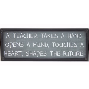 May include: A black framed sign with a gray background and white text that reads: "A teacher takes a hand, opens a mind, touches a heart, shapes the future."