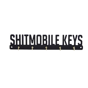 May include: Black metal key holder with the text "Shitmobile Keys" and five hooks.
