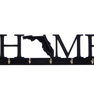 May include: Black metal key holder with the word "HOME" and an outline of the state of Florida. The holder has five hooks for hanging keys.