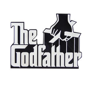 May include: A black and white sign featuring the text "The Godfather" in a bold, stylized font. The design includes a hand manipulating puppet strings, a classic visual from the film.