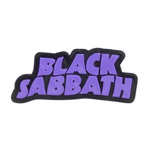 May include: A rectangular, black and purple Black Sabbath logo. The text "BLACK SABBATH" is in a bold, purple font, outlined in black. The logo is on a white background.