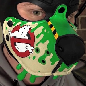 Peut inclure: Une cagoule noire avec un museau vert et beige orn&eacute; du logo Ghostbusters. Le museau pr&eacute;sente un fant&ocirc;me blanc dans un cercle rouge barr&eacute;, agr&eacute;ment&eacute; de motifs de slime vert et de bandes de signalisation noires et jaunes sur le dessus.