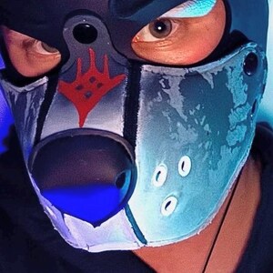 Peut inclure: Un masque cagoule inspir&eacute; d'un animal, noir et bleu, dot&eacute; d'un nez noir pro&eacute;minent, d'un symbole graphique rouge sur le front et de trois petits accents circulaires blancs sur le c&ocirc;t&eacute;. Le masque pr&eacute;sente une finition textur&eacute;e et des bordures noires.