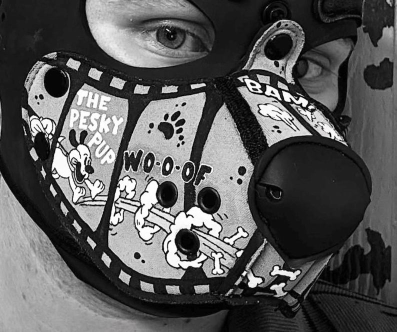 Peut inclure: Un masque animalier noir et blanc avec un imprim&eacute; style bande dessin&eacute;e portant les inscriptions THE PESKY PUP, WO-O-OF et BAM. Le masque comprend un embout nasal arrondi pro&eacute;minent, plusieurs &oelig;illets de ventilation circulaires et un motif graphique repr&eacute;sentant un chien qui court, des empreintes de pattes et des os.