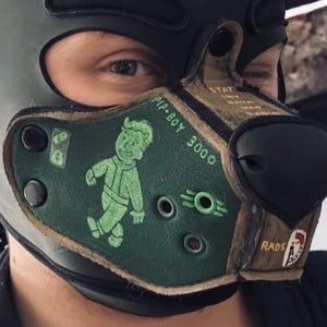 Peut inclure: Un masque museau en cuir vert fonc&eacute; et marron sur le th&egrave;me Fallout Pip-Boy 3000. Le masque pr&eacute;sente un graphique vert de Vault Boy, le texte PIP-BOY 3000, un symbole RADS et des &oelig;illets m&eacute;talliques. Il est fix&eacute; par des boutons-pression noirs.