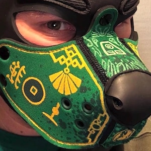 Peut inclure: Un masque museau de style animal vert et noir avec des motifs imprim&eacute;s jaunes, notamment un &eacute;ventail, une pi&egrave;ce circulaire et des formes g&eacute;om&eacute;triques. Le masque poss&egrave;de un nez noir, des &oelig;illets d'a&eacute;ration noirs et des rivets noirs.