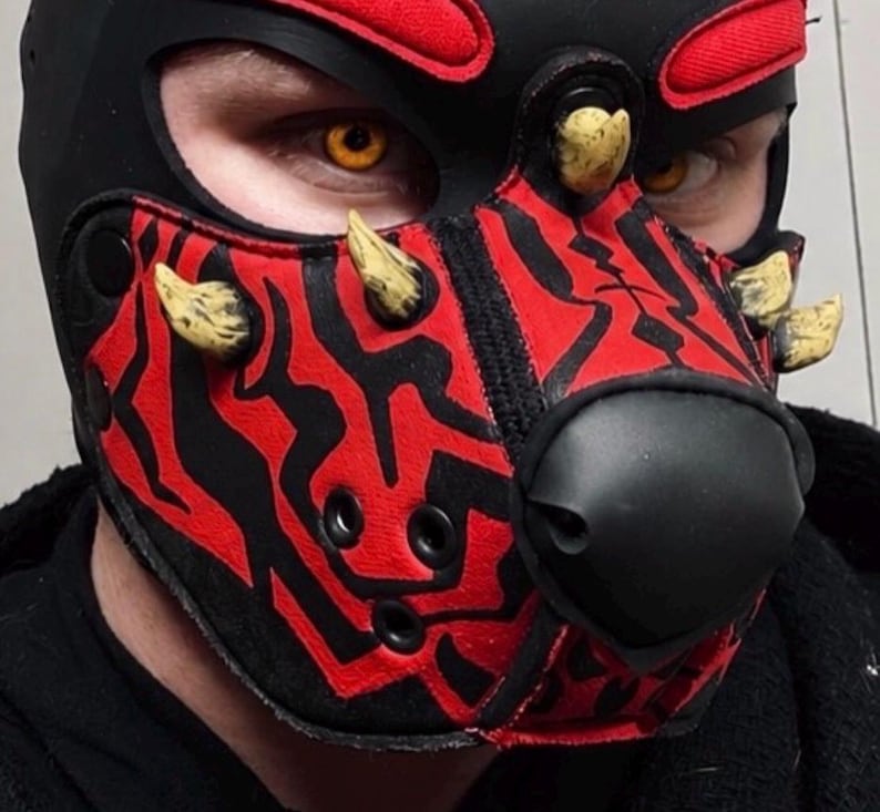 Peut inclure: Un masque cagoule &agrave; motifs noirs et rouges dot&eacute; d'un museau noir pro&eacute;minent, de plusieurs protub&eacute;rances beiges en forme de cornes et d'ouvertures pour les yeux. Le masque pr&eacute;sente un design rouge et noir dentel&eacute; sur le devant et le front.
