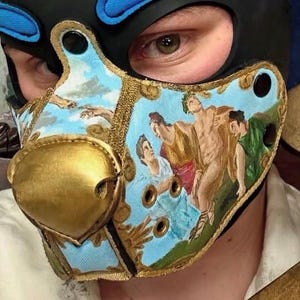 Peut inclure: Un masque cagoule noir dot&eacute; d'une pi&egrave;ce nasale dor&eacute;e pro&eacute;minente et d'un panneau facial bleu clair orn&eacute; d'une peinture classique repr&eacute;sentant des personnages et un ciel. Le masque comprend des &oelig;illets m&eacute;talliques dor&eacute;s et des boutons-pression noirs.