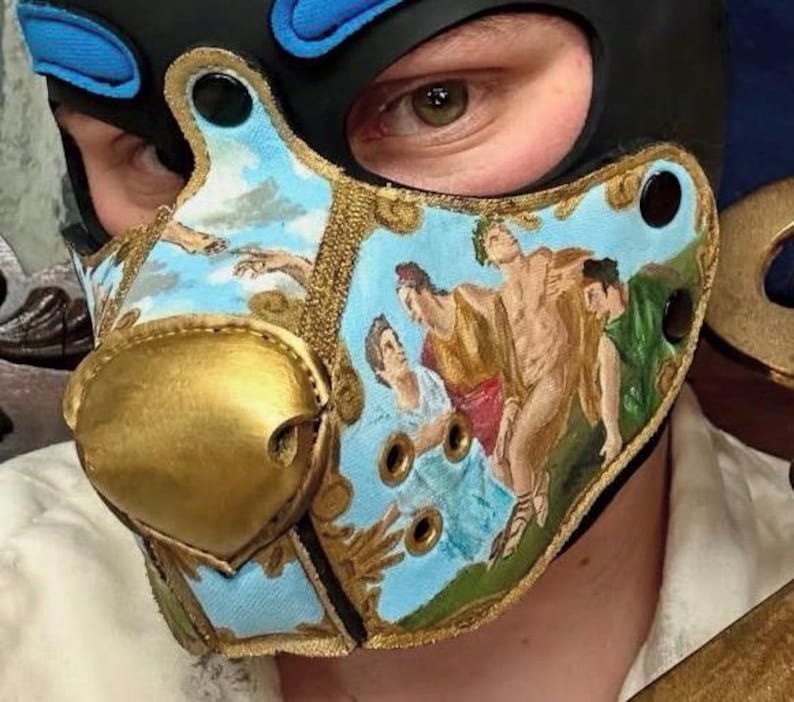 Peut inclure: Un masque cagoule noir dot&eacute; d'une pi&egrave;ce nasale dor&eacute;e pro&eacute;minente et d'un panneau facial bleu clair orn&eacute; d'une peinture classique repr&eacute;sentant des personnages et un ciel. Le masque comprend des &oelig;illets m&eacute;talliques dor&eacute;s et des boutons-pression noirs.