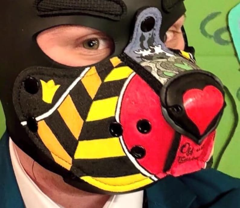 Peut inclure: Une cagoule noire dot&eacute;e d'un museau avec des rayures diagonales jaunes et noires, une section circulaire rouge et un nez en forme de c&oelig;ur. Le museau comprend des rivets noirs, un panneau sup&eacute;rieur d&eacute;coratif aux motifs gris et bleus et une bordure noire.