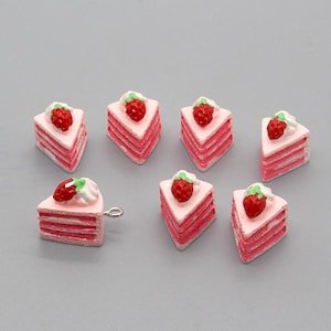 May include: Seven pink and white cake slices with a strawberry on top. Each slice has three layers of cake and a dollop of white frosting.