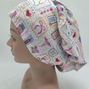 Puede incluir: Gorro quirúrgico blanco con un patrón repetido de diseños de sellos postales de temática médica. Los sellos presentan corazones, lazos, estetoscopios y la palabra "NURSE". El gorro está diseñado para ser usado en un entorno médico.