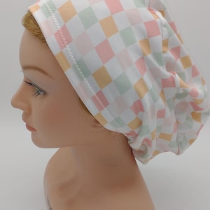 May include: A white, pink, green, and orange checkered scrub hat. The hat is made of a soft, stretchy fabric and has a comfortable fit.