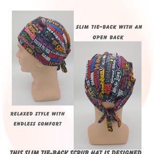 May include: A black tie-back scrub hat with a colorful print featuring band names and text. The hat has an open back and is designed to stay secure with comfort. The text on the hat includes "AC/DC" and "Faster Pussycat".