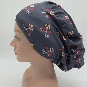May include: A dark gray cap with a floral pattern in red and cream colors. The cap is made of a soft fabric and is designed to fit snugly on the head. The floral design adds a touch of elegance.