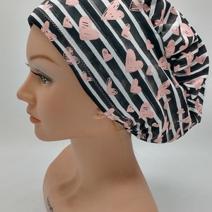 May include: A black and white striped scrub hat with pink hearts. The hat is made of a soft, comfortable fabric and has a stretchy fit.
