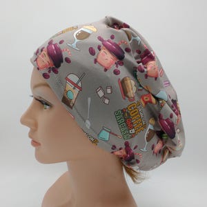 May include: A gray fabric cap with a repeating pattern of coffee-themed illustrations, including coffee cups, beans, and the text "I run on coffee and sarcasm." The cap is worn by a mannequin.
