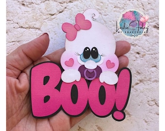 May include: Pink and white paper craft with the word "BOO!" in pink letters. A white baby ghost with a pink bow and pacifier is peeking out from behind the letters.