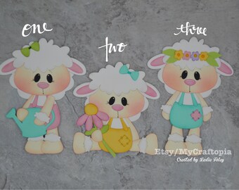 May include: Three paper craft lamb cutouts with different accessories. The first lamb is holding a watering can, the second is holding a flower, and the third is wearing a flower crown. The text "one", "two", and "three" is written above each lamb.