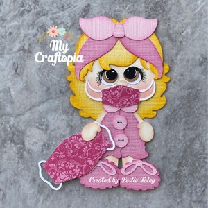 May include: A paper doll figure with blonde hair, a pink bow, and a pink dress. The doll wears a patterned face mask and holds a matching mask. The text "My Craftopia" and "Created by Leslie Foley" are visible.