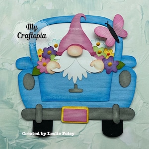 May include: A blue pickup truck with a gnome and flowers in the bed. A pink butterfly is perched on the side of the truck. The truck has a pink license plate with yellow lettering. The gnome is wearing a pink hat and has a white beard.
