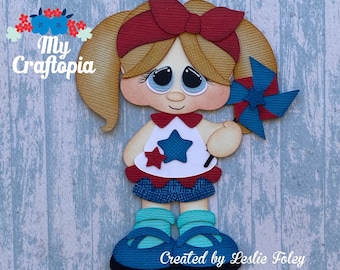 May include: Paper craft cutout of a girl with blonde pigtails wearing a red, white, and blue outfit and holding a blue and red pinwheel. The text "My Craftopia" is in the top left corner of the image. The text "Created by Leslie Foley Etsy/MyCraftopia" is in the bottom right corner of the image.