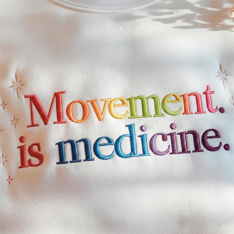 Pu&ograve; includere: Felpa bianca con la scritta ricamata "Movement. is medicine." nei colori dell'arcobaleno. Il testo &egrave; in grassetto, senza grazie. La felpa ha uno scollo tondo e un aspetto morbido e strutturato.