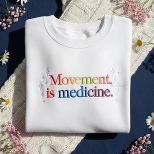 Pu&ograve; includere: Felpa bianca con la scritta ricamata "Movement is medicine" nei colori dell'arcobaleno. La felpa ha un girocollo ed &egrave; realizzata in materiale morbido. Il design include accenti a forma di stella.