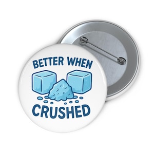 Op de afbeelding: Witte knoop met de tekst "BETTER WHEN CRUSHED" in blauw. Het ontwerp toont twee blauwe ijsblokjes en een hoop crushed ice. Een zilveren pinback is zichtbaar.