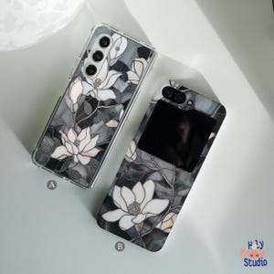 May include: Two phone cases with a black and white floral design. The cases feature a stained glass effect with white flowers on a black background. One case has a clear back and the other has a black back.