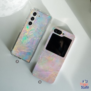 May include: Two phone cases with a pearlescent iridescent design. The case on the left is for a foldable phone and has a clear back. The case on the right is for a standard phone and has a black mirror on the front.