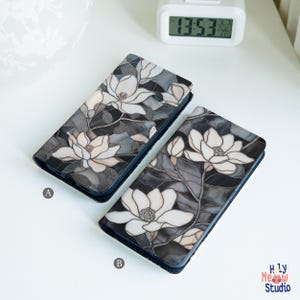 May include: Two rectangular phone cases labeled A and B, each featuring a stained glass-style pattern of white magnolia flowers with dark gray and black foliage. The designs are printed on a smooth surface, and the cases are positioned side by side.