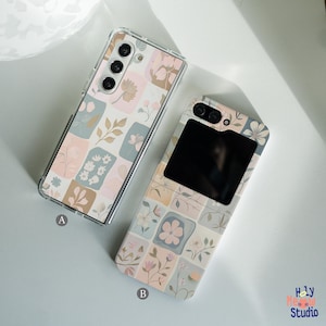 May include: Two phone cases with a floral pattern. The case on the left is for a foldable phone and has a clear back. The case on the right is for a standard phone and has a black mirror on the back. Both cases have a pastel pink, blue, and green color scheme.
