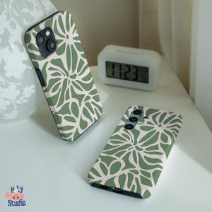 Könnte beinhalten: Zwei Handyhüllen mit einem grünen und weißen Blumenmuster. Die Hüllen sind aus hartem Kunststoff und haben eine matte Oberfläche.