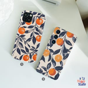 May include: Two phone cases with an orange and leaf design. The cases feature a cream background with orange fruit and dark blue leaves. One case is labeled "A" and the other is labeled "B". The cases are likely for a smartphone.
