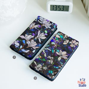 Può includere: Due custodie per telefono con un design a vetri colorati con fiori bianchi su sfondo blu scuro. Le custodie sono etichettate con A e B.