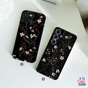 May include: Two black phone cases with a floral design. The cases feature a pattern of white flowers and thin, brown stems against a black background. One case has a dual-lens camera, and the other has a triple-lens camera.