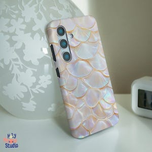 Puede incluir: Una funda de teléfono blanca con un patrón nacarado iridiscente. La funda tiene una lente de cámara triple en la parte posterior.