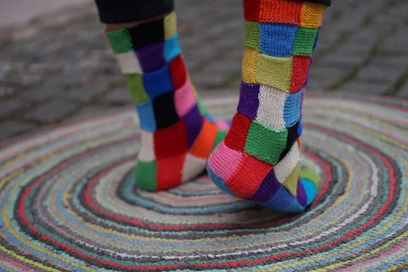 May include: A pair of colorful socks with a patchwork design. The socks are made of a soft, knitted fabric and feature a variety of bright colors, including red, blue, green, yellow, and purple.