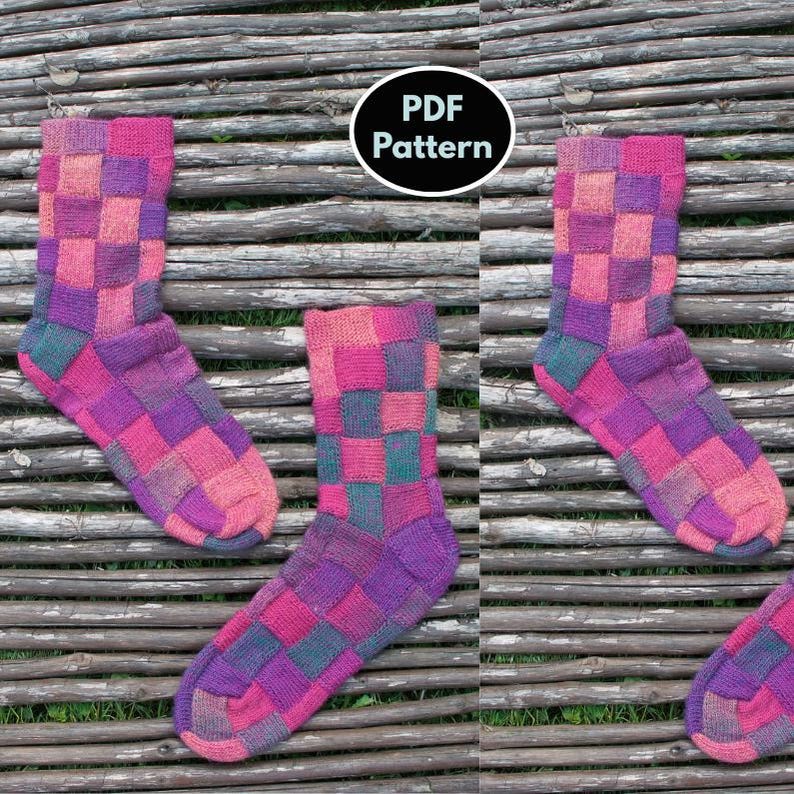 May include: A pair of knitted socks with a checkered pattern in shades of pink, purple, and green. The socks are displayed on a wooden surface. PDF Pattern.