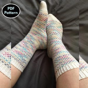 Puede incluir: Un par de calcetines coloridos con un patrón de puntada de panal. Los calcetines están hechos con un hilo blanco y tienen motas multicolores en todo. Los calcetines se muestran en las piernas de una persona.