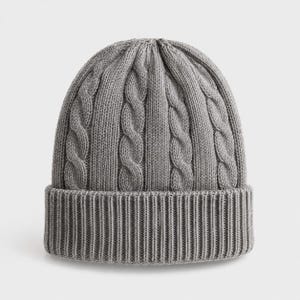 Peut inclure: Un bonnet en tricot gris présentant un motif de torsades verticales sur toute la calotte et un large revers côtelé à la base. Le bonnet est confectionné dans un fil gris uni, affichant une texture uniforme et une forme arrondie structurée.