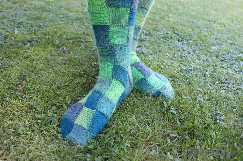 May include: A pair of colorful socks with a patchwork design in shades of green and blue. The socks are made of a soft, knitted fabric and have a comfortable fit.