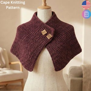 May include: A burgundy knitted cape with two square wooden buttons. The cape is displayed on a mannequin. The text "Cape Knitting Pattern" is visible in the upper left corner. The American flag and a PDF icon are in the upper right corner.